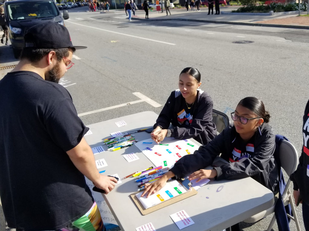 Two youth running a signup table outside with colorful stickers