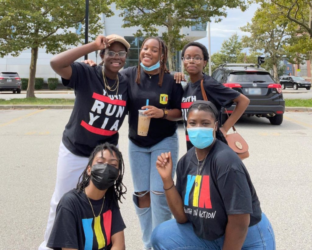 Five people wearing Youth in Action tshirts posing in a parking lot