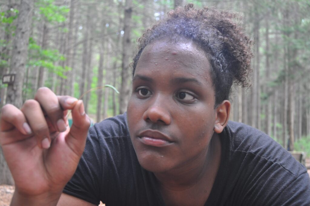 A teenager looks closely at a small piece of a plant in their hand.